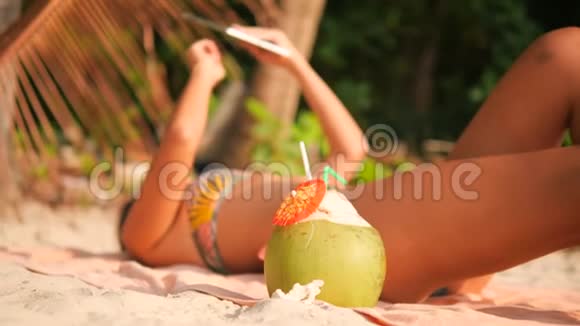比基尼的年轻旅游妇女躺在热带天堂沙滩上享受日光浴并使用移动平板小玩意4K视频的预览图