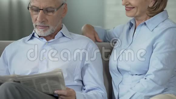 一个坐在沙发上看报纸的老人一个坐在他身边的女人在关心他视频的预览图