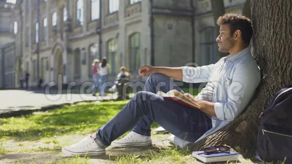 跨国公司的家伙坐在树下看书四处张望闲暇时间视频的预览图