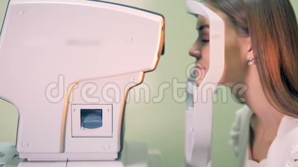 旁边看到一位年轻女士把头放在医疗机器上检查她的眼睛视频的预览图