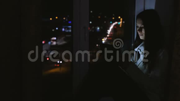 女人在平板电脑上玩游戏在黑暗中坐在窗台上视频的预览图