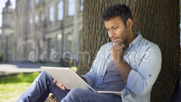 混血年轻人在笔记本电脑上聊天坐在树下约会网站视频的预览图