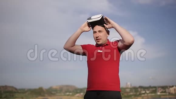 在蓝天背景下男人在公园里用VR眼镜训练拳击视频的预览图