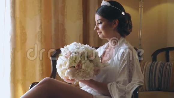 年轻的新娘坐在一家豪华酒店的窗边手里拿着一束鲜花视频的预览图