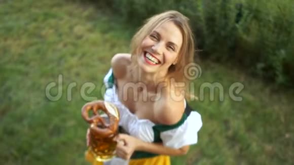 节日啤酒节一个穿着巴伐利亚西装手里拿着一大杯啤酒和椒盐卷饼的女人欢快地笑着视频的预览图