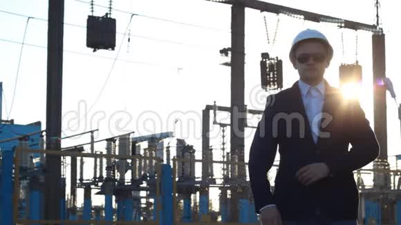 一个戴着白色头盔和黑色眼镜的人站在电站的背景下双臂交叉交叉日落视频的预览图