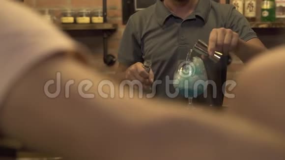 酒保在咖啡馆的酒吧柜台用冰和蓝色的酒做酒精鸡尾酒巴曼在冰上倒酒视频的预览图