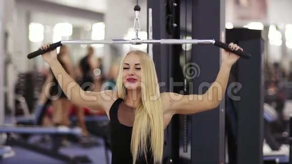 漂亮的白种人年轻的金发女人在健身房里用拉制的马什琴锻炼时身体健康面带微笑视频的预览图