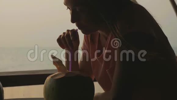 年轻女子坐在海景咖啡厅慢动作喝椰子水视频的预览图