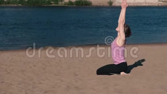 在城市河边的海滩上伸展瑜伽的女人美丽的城市景色呼吸练习视频的预览图