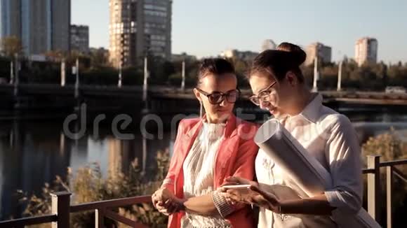 两个女孩的建筑师站在河边讨论建设项目商业建筑视频的预览图