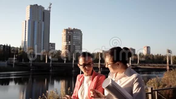 两个女孩的建筑师站在河边讨论建设项目商业建筑视频的预览图