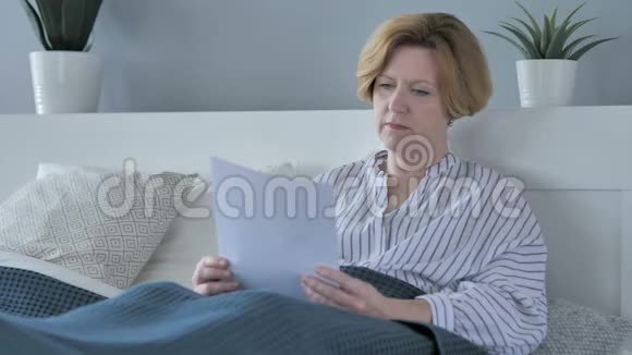 老年妇女在床上阅读文件纸制品视频的预览图