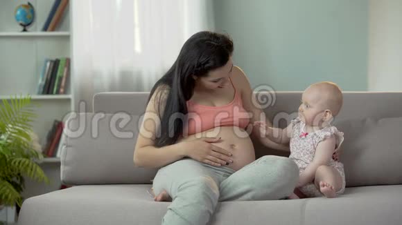 可爱的宝贝女孩在大肚子上拍着孕妈妈快乐的分娩视频的预览图