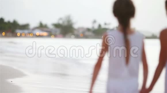美丽的小女孩和年轻的母亲在美丽的夕阳下漫步在海滩上视频的预览图