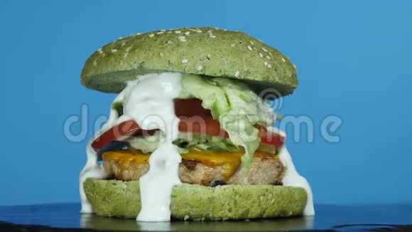 孤立的汉堡包在蓝色背景上旋转大汉堡有肉馅饼和绿色面包洋葱番茄融化的奶酪视频的预览图