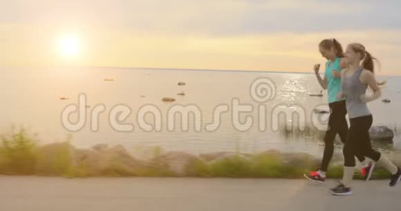 傍晚日落时分两个女孩在海边的人行道上奔跑视频的预览图