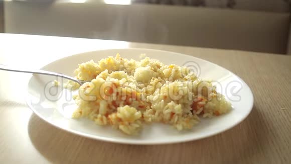 一个男人在家里的一张木桌上用一个叉子和一个白色盘子里的鸡肉吃米饭视频的预览图