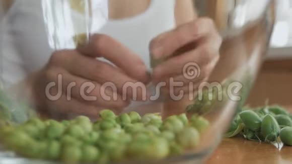 坐在桌子旁的女人拿出新鲜的绿色鹰嘴豆放进一个玻璃碗里视频的预览图