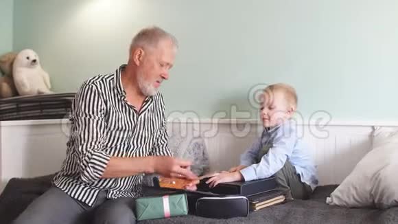 一代人祖父和孙子带着礼品盒坐在家里的沙发上视频的预览图