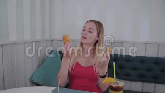 漂亮的女孩摆姿势手里拿着甜甜圈在咖啡馆的桌子上视频的预览图