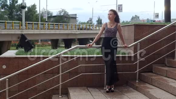 孤独的漂亮女孩站在楼梯上风在城市的街道上流着头发视频的预览图