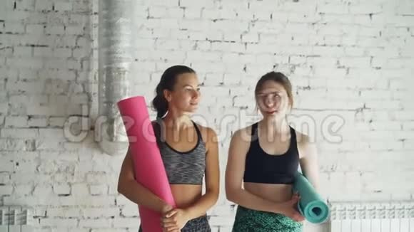 多莉拍摄了两个年轻的女人穿着时髦的运动服在瑜伽工作室里散步铺着五颜六色的垫子和谈话女孩视频的预览图