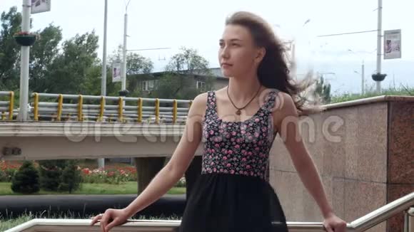 孤独的漂亮女孩站在楼梯上风在城市的街道上流着头发视频的预览图