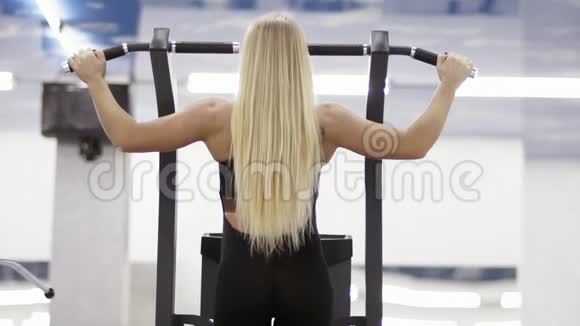 强壮的女性健美运动员金发肌肉发达的手臂在健身房的水平杆上拉起来视频的预览图