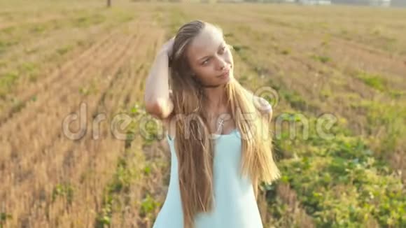 黄昏时分一个16岁的女孩站在田野里留着长发和一件蓝色连衣裙的肖像视频的预览图