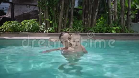 可爱的小孩和他妈妈在游泳池里上游泳课母亲双手握着她的背景视频的预览图