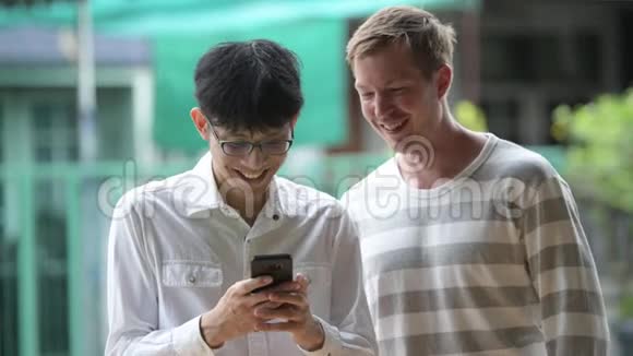 两个快乐的多民族商人在户外的街道上一起用电话微笑视频的预览图