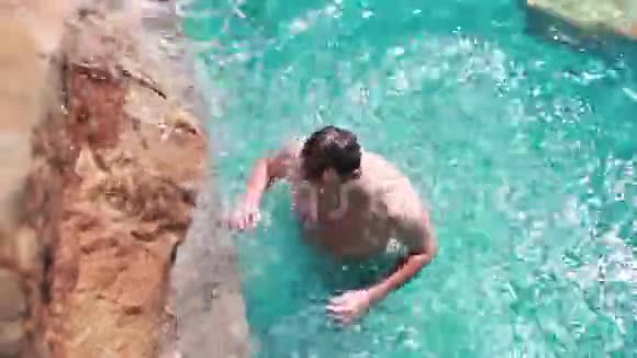 从顶部看当一个人放松在游泳池有淋浴瀑布在晴天1920x1080视频的预览图