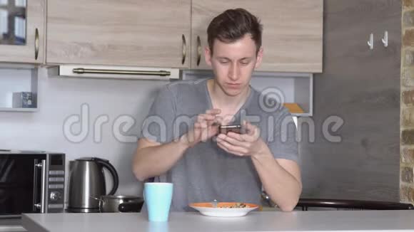 有电话的年轻人在厨房的桌子旁吃饭视频的预览图