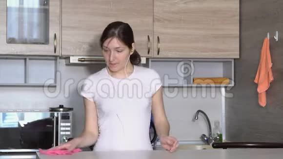 美丽的女人正在厨房里打扫卫生随着耳机里的音乐跳舞视频的预览图