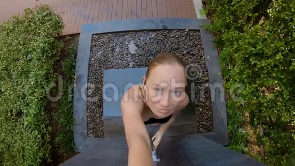 一个年轻女人在热带花园里洗澡的慢镜头在热带度假胜地度假的概念年轻女子视频的预览图