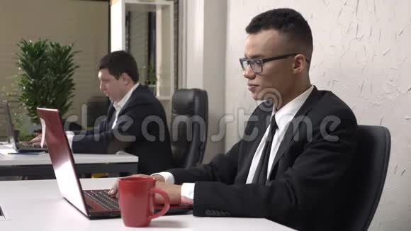 年轻成功的非洲商人戴着眼镜坐在办公室里手提电脑喝着一杯咖啡视频的预览图