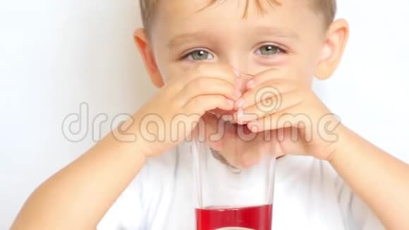 一个小孩在白色背景下喝着玻璃烧杯里的果汁然后他微笑着特写镜头视频的预览图