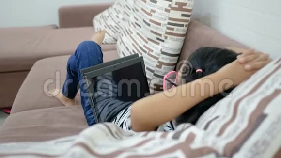 亚洲小女孩躺在沙发上用平板电脑放松视频的预览图