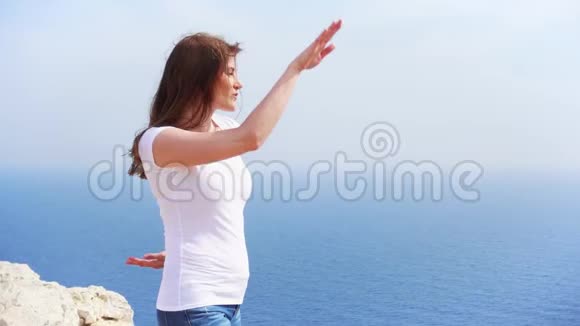 阳光明媚的一天女人在悬崖上与蔚蓝的大海欢快地跳跃无护理女性慢动作舞蹈视频的预览图