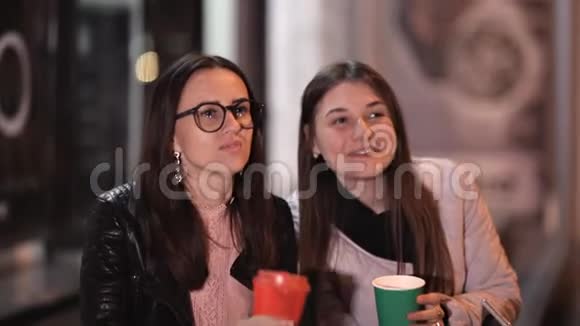 两个年轻女孩晚上穿过老城聊天喝热咖啡视频的预览图