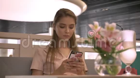 年轻漂亮的女孩坐在rastaurant里在智能手机上聊天喝咖啡放松概念交流视频的预览图