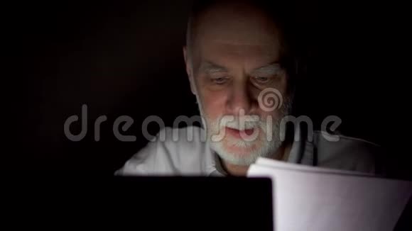 疲惫的资深商人在深夜用笔记本电脑工作只有一张漆黑的脸视频的预览图