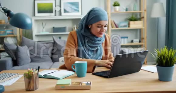 戴头巾的独立女孩自由职业者在公寓里用笔记本电脑工作视频的预览图