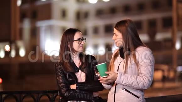两个年轻女孩晚上穿过老城聊天喝热咖啡视频的预览图