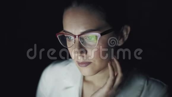 戴眼镜的女人在黑暗中在笔记本电脑上工作一个女孩晚上在电脑上消磨时间的肖像视频的预览图