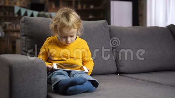 可爱的金发幼儿男孩在沙发上使用触摸板视频的预览图