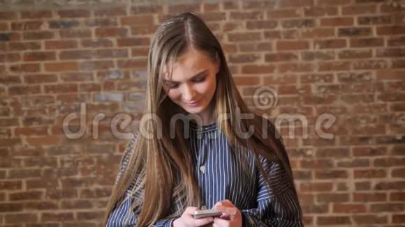 年轻漂亮的女孩正在看她的智能手机微笑交流概念放松概念砖背景视频的预览图