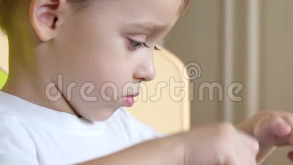 一个脸严肃的孩子坐在桌子旁触摸平板电脑的触摸屏视频的预览图