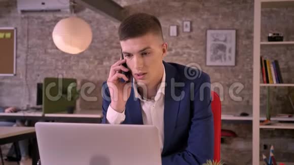 年轻的严肃商人在智能手机上交谈与笔记本电脑合作交流理念商业理念视频的预览图